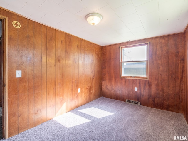 empty room with wood walls, visible vents, and carpet floors