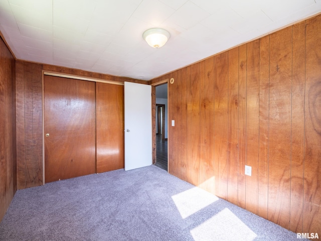 unfurnished bedroom with wood walls, a closet, and carpet