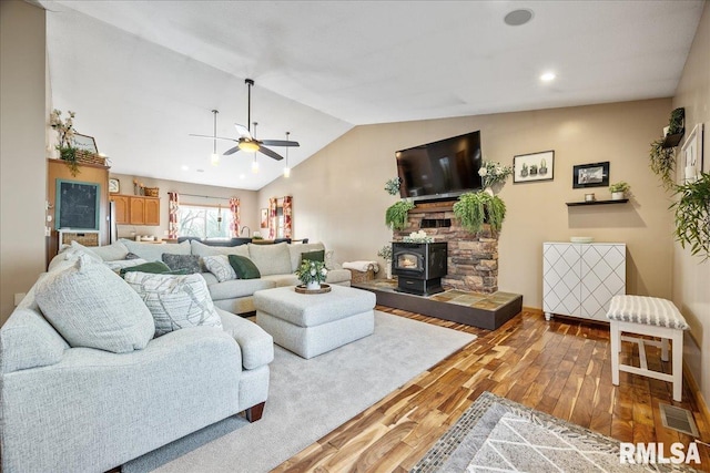 living area featuring a wood stove, lofted ceiling, a ceiling fan, visible vents, and wood finished floors