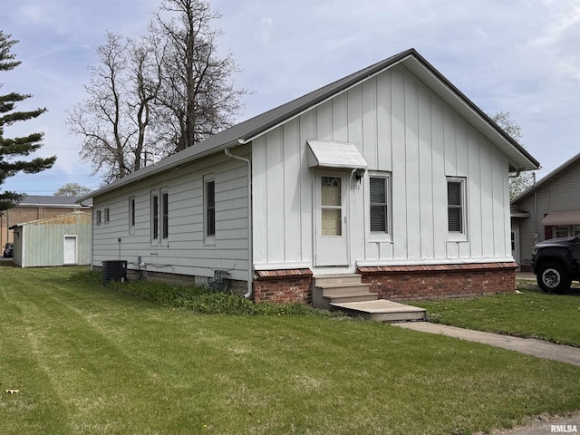 view of front facade with entry steps, central AC unit, board and batten siding, and a front yard