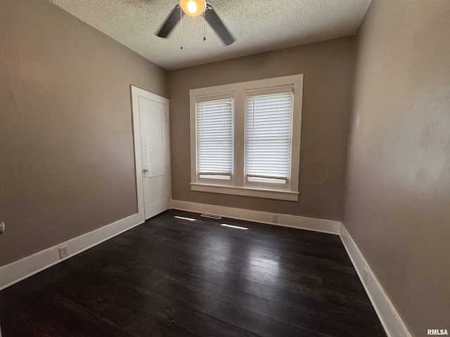 empty room featuring dark wood-type flooring, a ceiling fan, and baseboards
