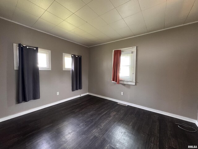 empty room with crown molding, visible vents, dark wood-style floors, and a healthy amount of sunlight