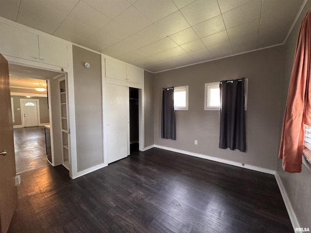 unfurnished bedroom featuring dark wood-type flooring, ornamental molding, baseboards, and a closet