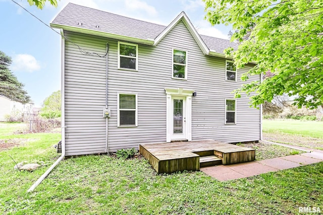 rear view of house with roof with shingles, a wooden deck, and a lawn