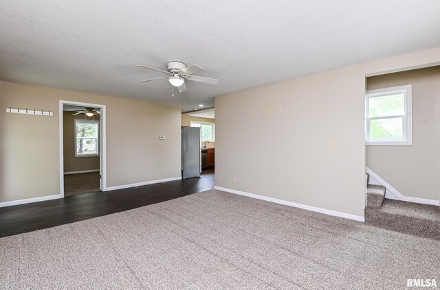 spare room featuring a ceiling fan, a wealth of natural light, dark colored carpet, and stairs