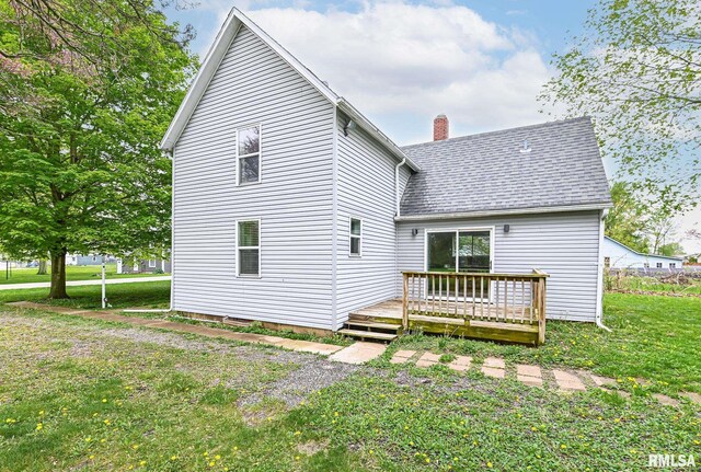 rear view of property featuring a shingled roof, a yard, a chimney, and a wooden deck