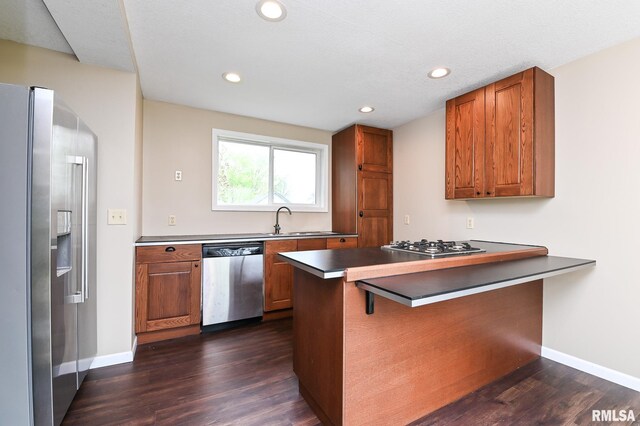 kitchen with dark wood-style flooring, stainless steel appliances, a peninsula, and brown cabinets