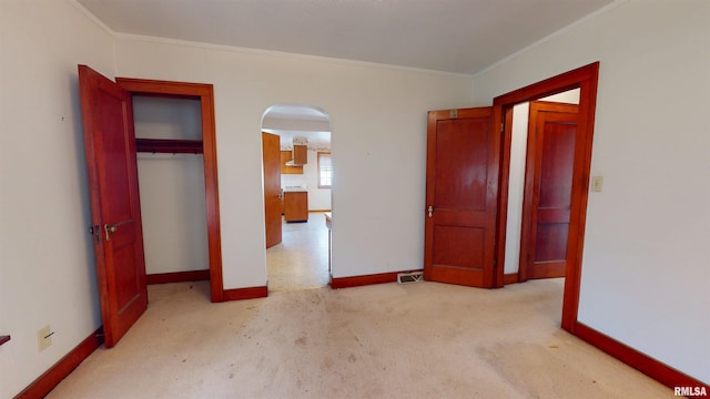 unfurnished bedroom with crown molding, carpet flooring, arched walkways, baseboards, and a closet