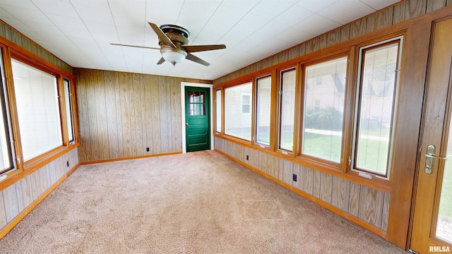 carpeted spare room with wooden walls, a ceiling fan, and baseboards