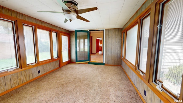 unfurnished sunroom with baseboards, carpet flooring, and wood walls