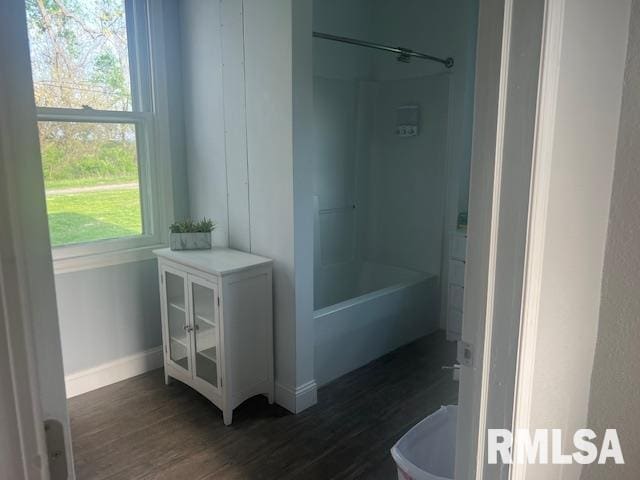 bathroom featuring baseboards, wood finished floors, and shower / washtub combination