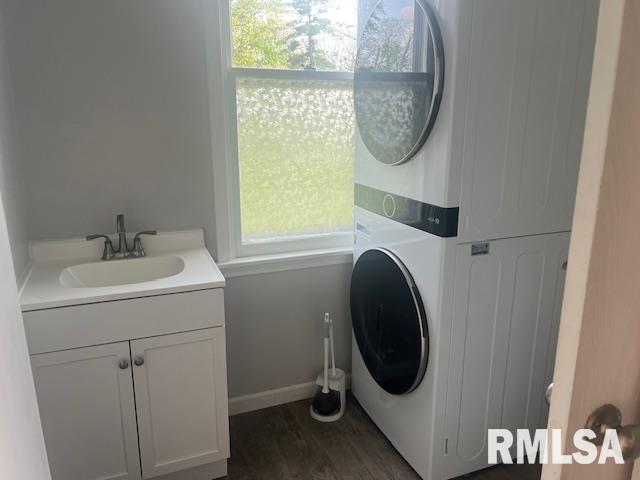 laundry room with cabinet space, stacked washer / drying machine, a sink, baseboards, and dark wood-type flooring