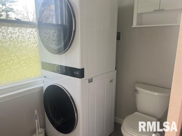 bathroom with stacked washer / drying machine and toilet