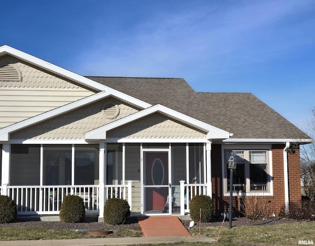 view of front of house featuring brick siding, a shingled roof, and a sunroom