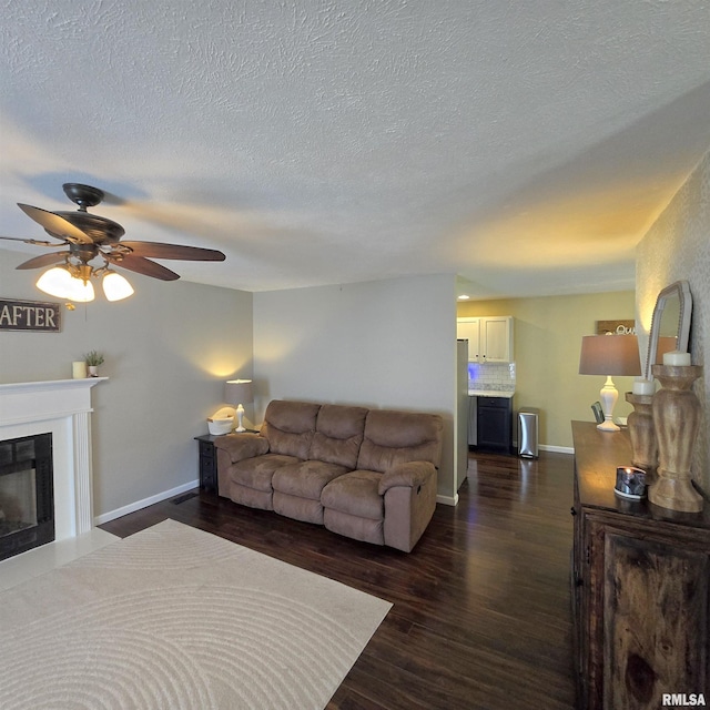 living area with a textured ceiling, dark wood finished floors, a ceiling fan, baseboards, and a fireplace with flush hearth