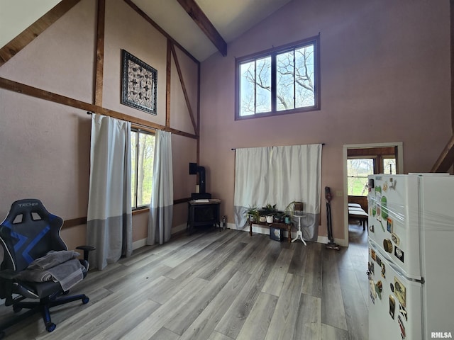 interior space with a wood stove, beam ceiling, high vaulted ceiling, baseboards, and light wood-style flooring