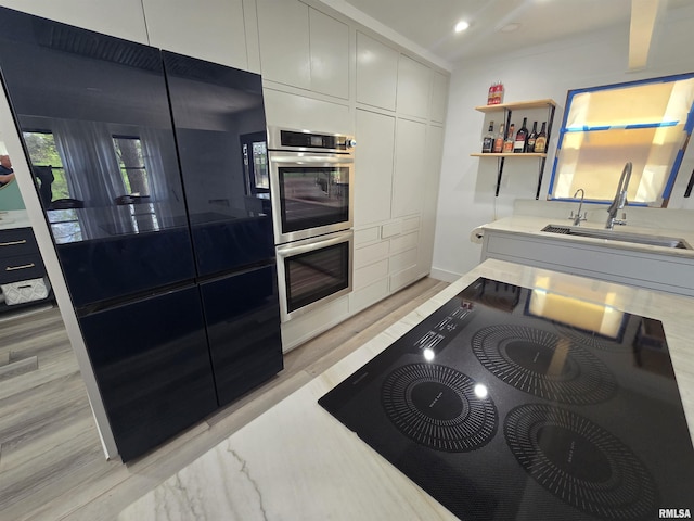 kitchen featuring stainless steel double oven, a sink, light countertops, black electric stovetop, and recessed lighting