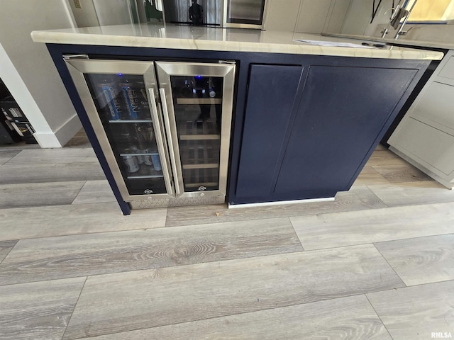 interior space featuring blue cabinetry, light wood-type flooring, light countertops, beverage cooler, and glass insert cabinets