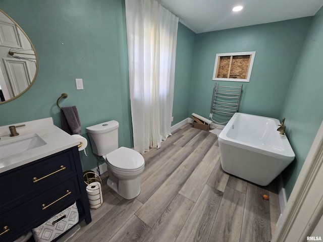full bathroom featuring toilet, a freestanding tub, wood finished floors, and vanity