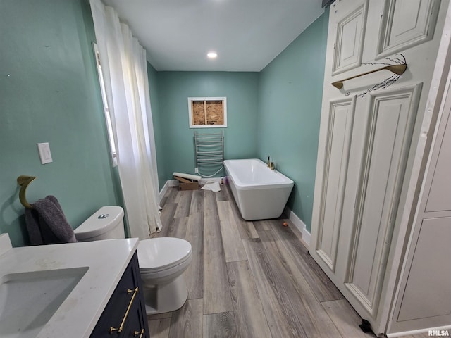 bathroom with baseboards, a freestanding tub, wood finished floors, and toilet