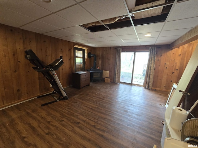 workout area featuring wooden walls, a wood stove, dark wood-style flooring, and a wealth of natural light