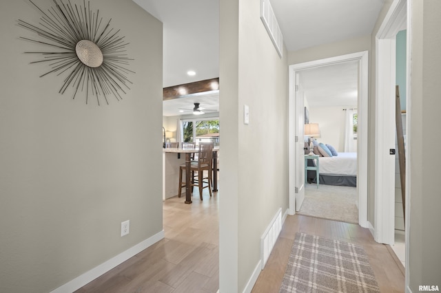 hallway featuring baseboards, visible vents, and light wood finished floors