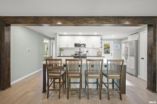 kitchen with appliances with stainless steel finishes, decorative backsplash, beam ceiling, and light wood finished floors