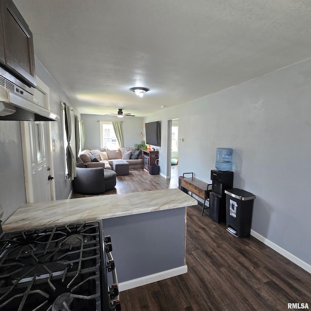 kitchen featuring dark wood-type flooring, light countertops, baseboards, and under cabinet range hood