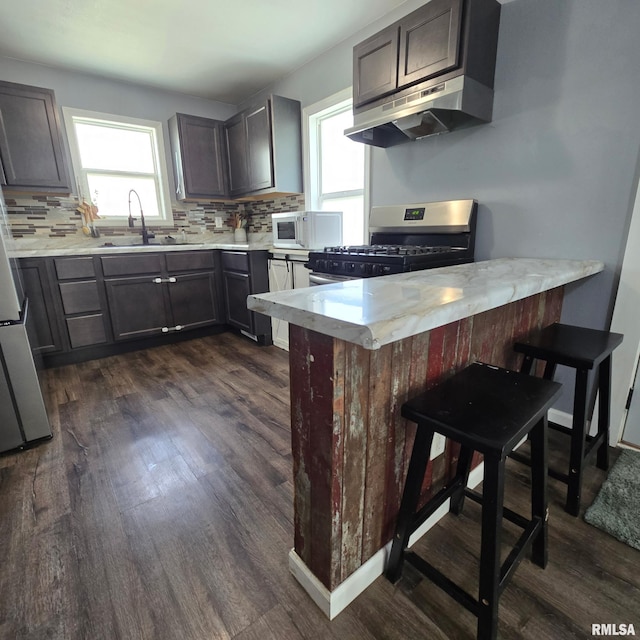 kitchen featuring stainless steel range with gas stovetop, dark wood finished floors, a sink, white microwave, and under cabinet range hood