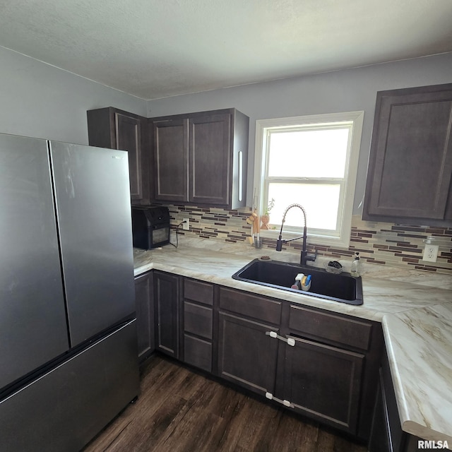 kitchen with freestanding refrigerator, dark wood-style flooring, a sink, and tasteful backsplash
