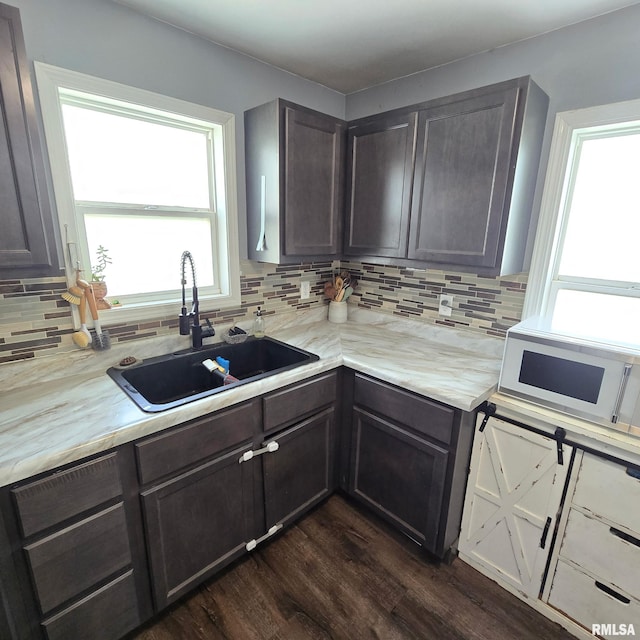 kitchen with decorative backsplash, a sink, light countertops, white microwave, and dark wood-type flooring