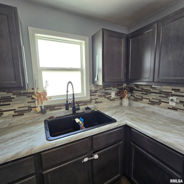 kitchen with backsplash, dark brown cabinetry, a sink, and light countertops