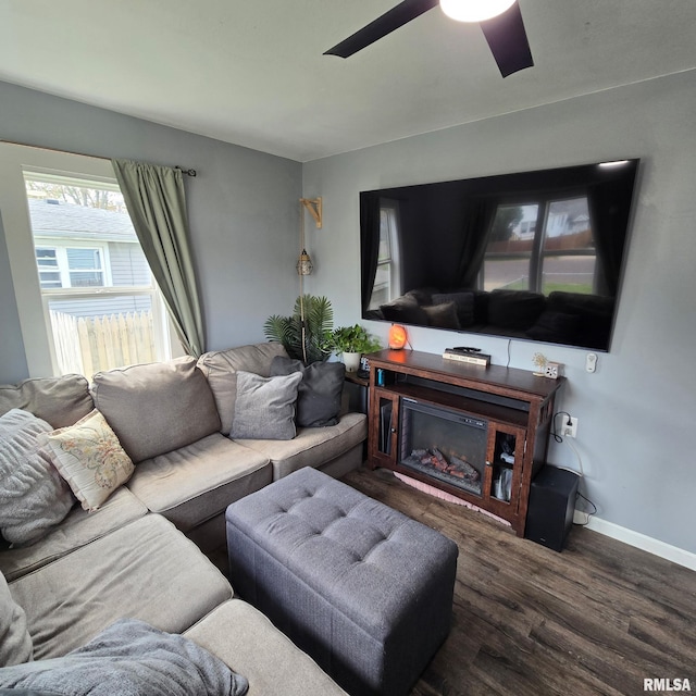 living room featuring baseboards, a ceiling fan, a glass covered fireplace, and wood finished floors