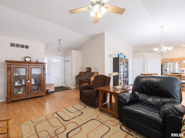 living area with lofted ceiling, ceiling fan with notable chandelier, visible vents, light wood finished floors, and baseboards