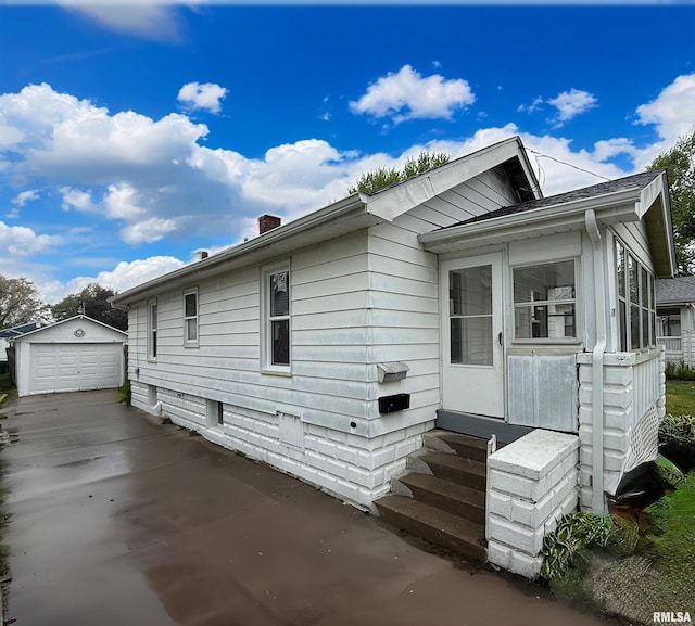 exterior space featuring driveway, a chimney, a detached garage, an outdoor structure, and entry steps