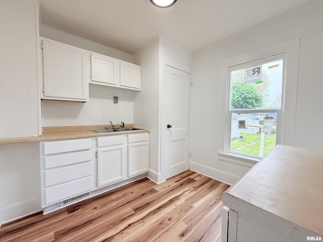 kitchen featuring light countertops, white cabinetry, a sink, and light wood-style flooring