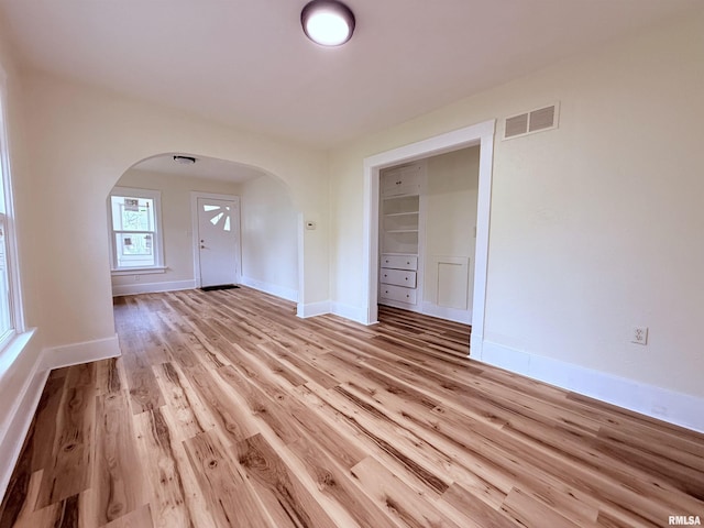 spare room featuring light wood-style floors, arched walkways, baseboards, and visible vents