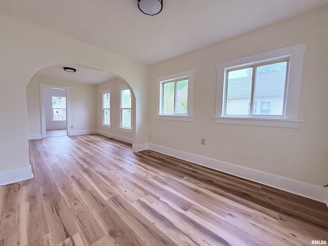 unfurnished living room featuring arched walkways, baseboards, and light wood-style flooring