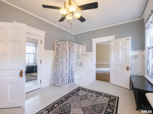 interior space with crown molding, wainscoting, shower / bath combo with shower curtain, a ceiling fan, and tile walls