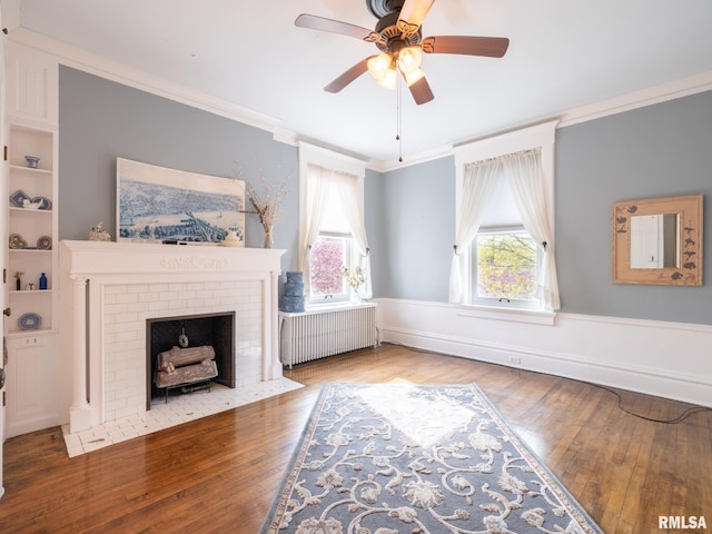 unfurnished living room with a ceiling fan, crown molding, a brick fireplace, wood finished floors, and radiator