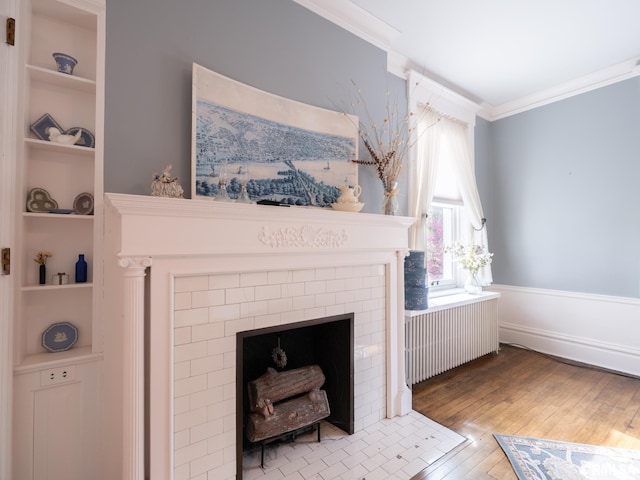 living area with a fireplace, built in shelves, wood-type flooring, radiator, and ornamental molding
