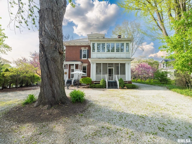 view of front of property with a chimney, a sunroom, and brick siding