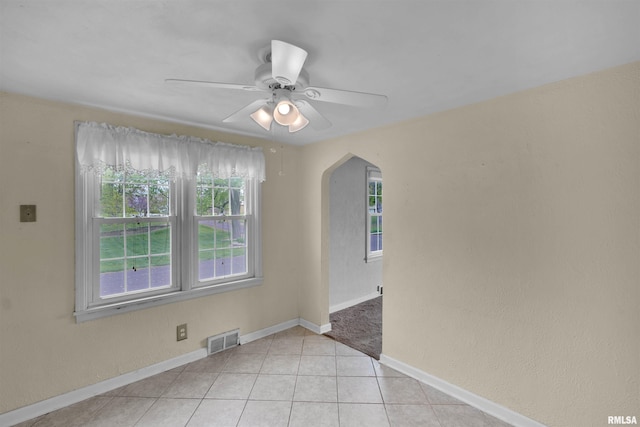 unfurnished room featuring arched walkways, a ceiling fan, baseboards, light tile patterned floors, and visible vents