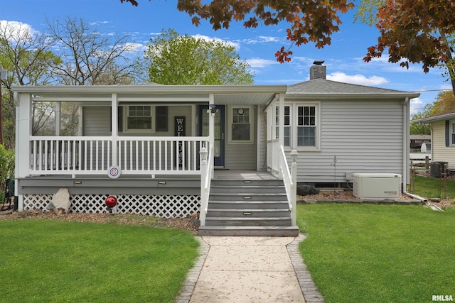 view of front facade featuring a porch, a chimney, a shingled roof, and a front yard