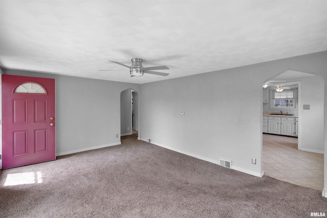 unfurnished living room with ceiling fan, light carpet, a sink, arched walkways, and visible vents