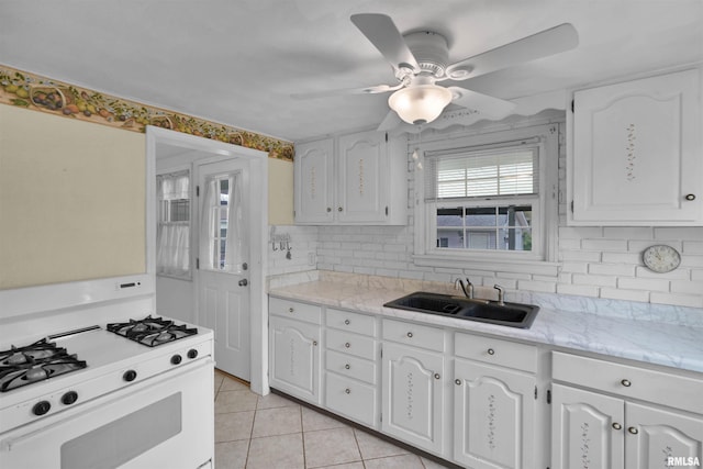 kitchen featuring gas range gas stove, white cabinets, a sink, backsplash, and light tile patterned floors