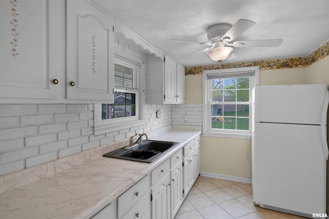 kitchen featuring freestanding refrigerator, decorative backsplash, light countertops, white cabinetry, and a sink