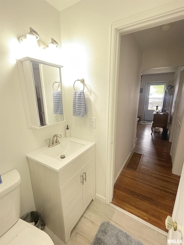 half bath featuring visible vents, vanity, wood finished floors, toilet, and baseboards