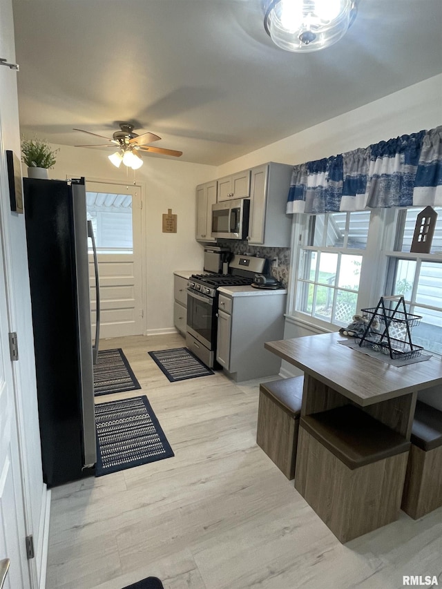 kitchen with ceiling fan, light wood-type flooring, gray cabinets, tasteful backsplash, and appliances with stainless steel finishes