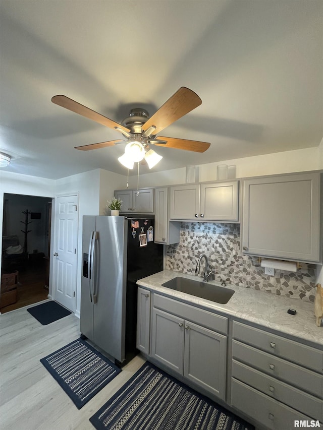 kitchen with gray cabinets, a ceiling fan, stainless steel refrigerator with ice dispenser, tasteful backsplash, and a sink